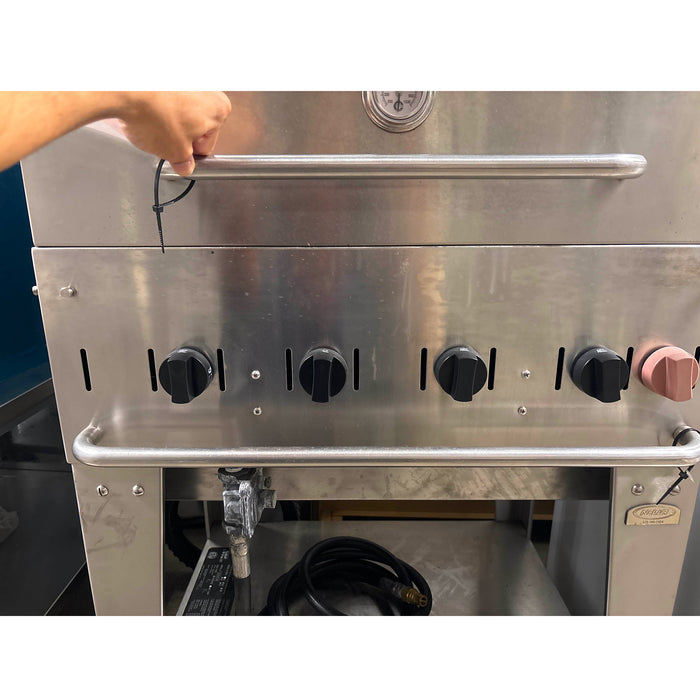 Stainless steel commercial oven with control knobs and a person's hand on the door handle.