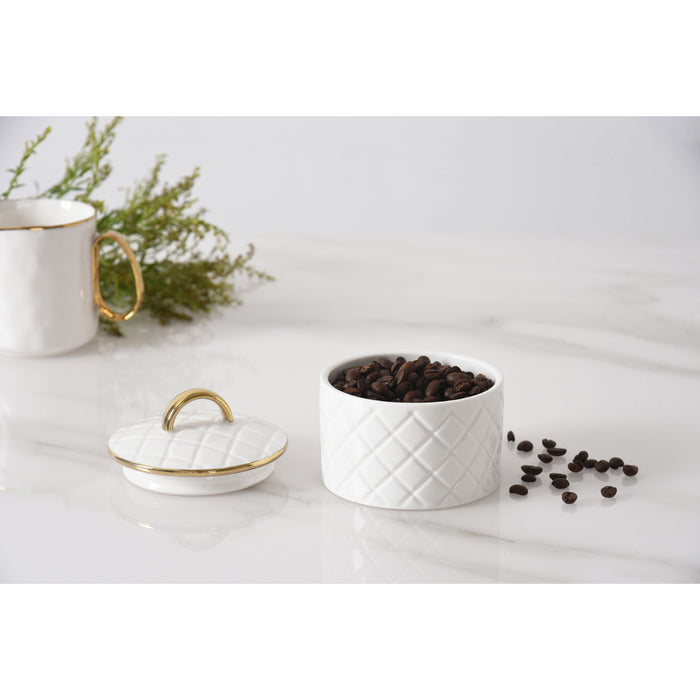 A white small canister with a diamond-quilted pattern and a matching lid, accented with gold trim, shown on a white marble surface with coffee beans scattered nearby.