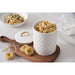 A white large canister with a diamond-quilted pattern and gold trim, shown filled with fettuccine on a wooden board. The matching lid sits beside it, with a bowl of pasta and a crumpled napkin in the background on a light marble surface.