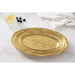 An oval gold serving platter with a textured, concentric-ring pattern, styled on a white marble surface with a glass of lemon water, blueberries, and a white napkin.