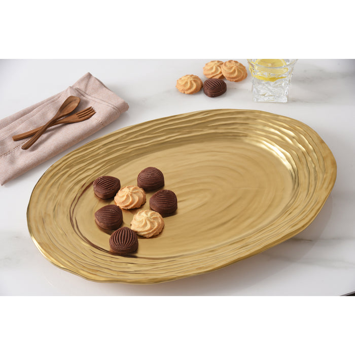 A large oval gold serving platter with a textured pattern, styled on a white marble surface with chocolate truffles, cookies, a napkin, and wooden cutlery.