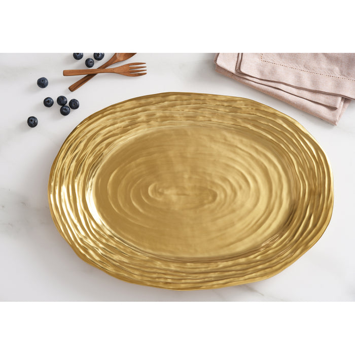 A large oval gold platter with a textured styled on a white marble surface with blueberries, wooden forks, and a folded napkin.
