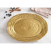 A large oval gold platter with a textured styled on a white marble surface with blueberries, wooden forks, and a folded napkin.