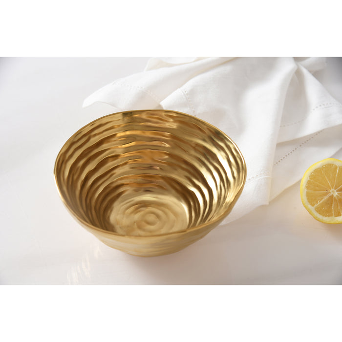 A gold bowl with a concentric wave texture, styled on a white surface next to a white napkin and a lemon slice.
