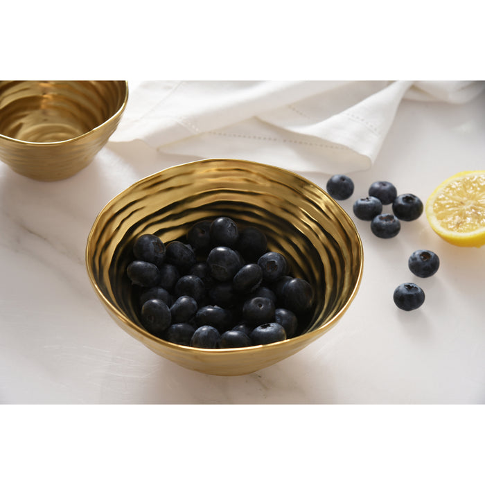 A gold bowl filled with blueberries on a white marble surface, with a second bowl partially visible in the background and a lemon half nearby.