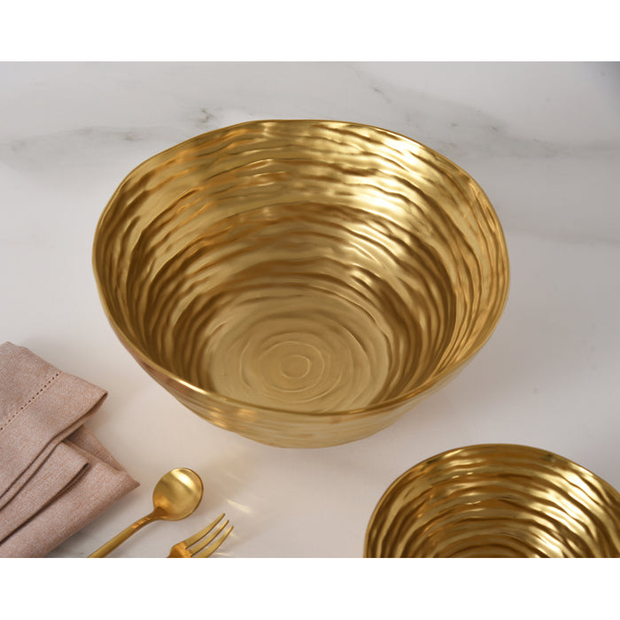 A large gold bowl with a matching spoon and fork, alongside a folded beige napkin, arranged on a white marble surface.
