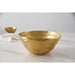 A gold salad serving bowl with an organic, wavy rim, displayed on a white marble surface with a soft-focus background showing a matching bowl and a white cloth.