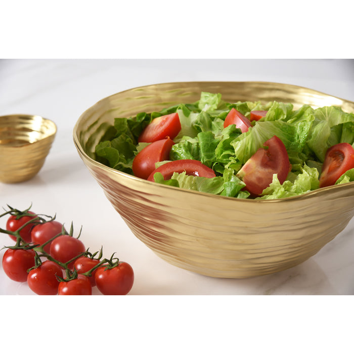 A large gold salad serving bowl filled with a green salad of lettuce and tomato slices, shown on a light surface with a small matching gold bowl and cherry tomatoes in the background.