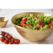 A large gold salad serving bowl filled with a green salad of lettuce and tomato slices, shown on a light surface with a small matching gold bowl and cherry tomatoes in the background.