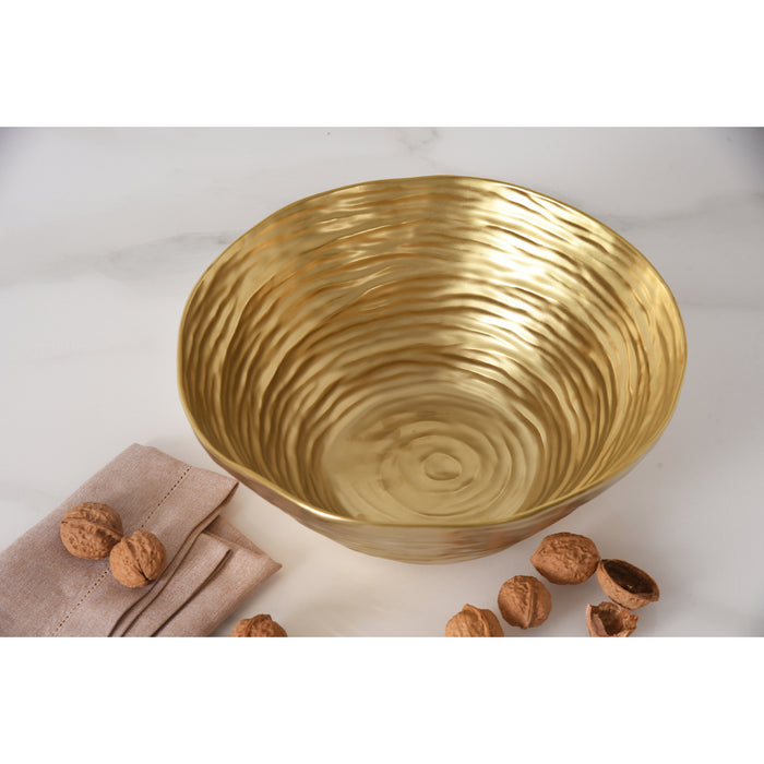 A large gold salad serving bowl with a textured, concentric ripple pattern, styled on a white marble surface with walnuts and a beige linen napkin.