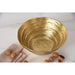 A large gold salad serving bowl with a textured, concentric ripple pattern, styled on a white marble surface with walnuts and a beige linen napkin.
